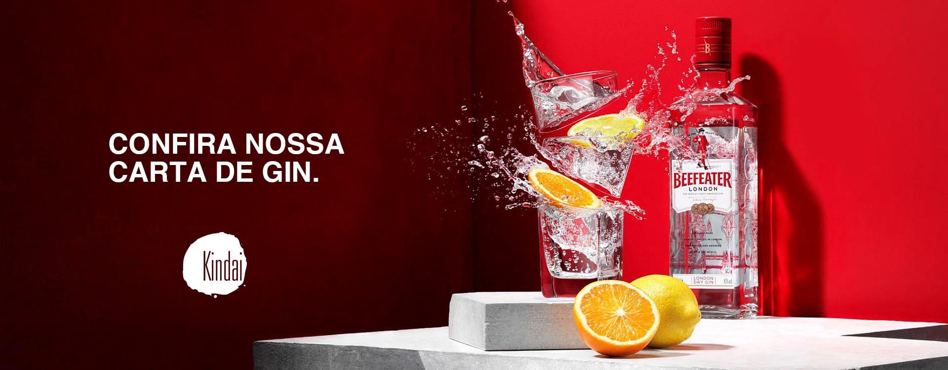 Uma garrafa de gim Beefeater fica ao lado de um copo com respingos de gim, gelo e fatias de laranja. As metades de limão e laranja estão sobre um bloco de concreto. O texto em português diz "Confira nossa carta de gim". Fundo vermelho.